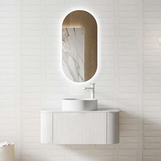Minimalist wall-mounted vanity in matte white with a ribbed texture and a round above-counter ceramic basin. Paired with an oval LED mirror featuring a unique marble and wood panel backdrop for a modern, luxurious look.
Elegant white vanity with ribbed detailing, a porcelain countertop, and a round above-counter ceramic basin. Complemented by an oval LED mirror with a single touch switch, ideal for sleek and modern bathroom designs.