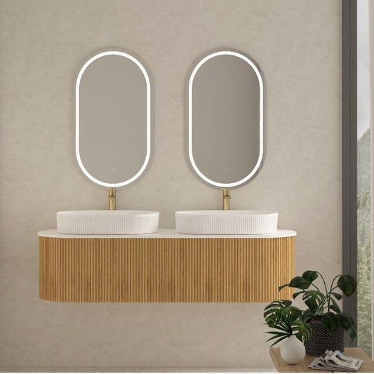 Elegant double vanity with a ribbed walnut wood finish and two oval above-counter ceramic basins, paired with dual oval LED mirrors. Set against a neutral wall with natural light and indoor plants for a refreshing and modern aesthetic.
Contemporary walnut wood double vanity featuring soft-closing drawers, a pure white porcelain countertop, and two oval above-counter ceramic basins. Paired with functional LED mirrors, combining practicality and style for modern bathrooms.