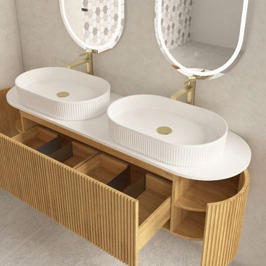 Elegant double vanity with a ribbed walnut wood finish and two oval above-counter ceramic basins, paired with dual oval LED mirrors. Set against a neutral wall with natural light and indoor plants for a refreshing and modern aesthetic.
Contemporary walnut wood double vanity featuring soft-closing drawers, a pure white porcelain countertop, and two oval above-counter ceramic basins. Paired with functional LED mirrors, combining practicality and style for modern bathrooms.