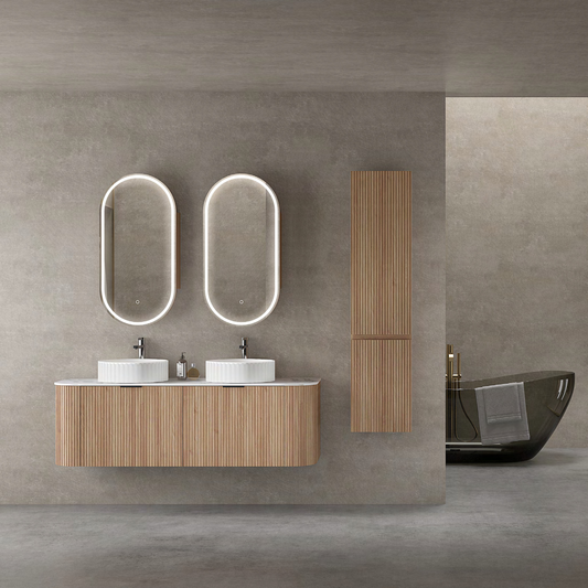 Modern double vanity set with ribbed wooden cabinets, dual round above-counter ceramic basins, and two vertical oval LED mirrors. Complemented by a matching tall storage cabinet, set against a neutral concrete-toned wall.
Stylish ribbed wooden vanity featuring a Carrara porcelain slab countertop, a round ceramic basin, and an oval LED mirrored shaving cabinet with functional storage. The minimalist design is highlighted by a clean, white-tiled background.
Elegant wooden vanity with a ribbed finish, Carrara