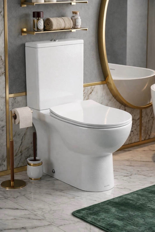 A modern white ceramic toilet in a luxurious bathroom setting with gold fixtures, a marble wall, a round gold-framed mirror, and a green bath rug.