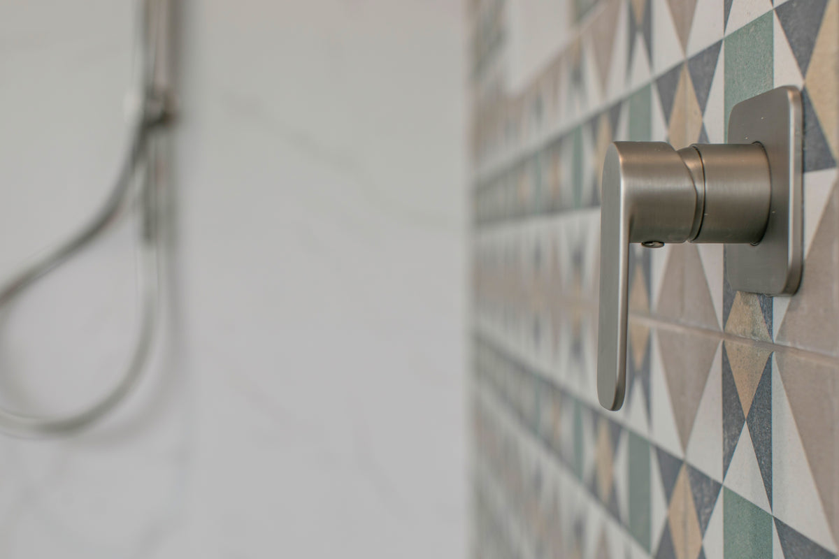 Close-up of a brushed nickel shower mixer mounted where the marble-look tile meets the patterned geometric feature tile
