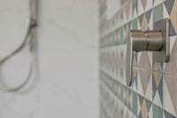 Close-up of a brushed nickel shower mixer mounted where the marble-look tile meets the patterned geometric feature tile