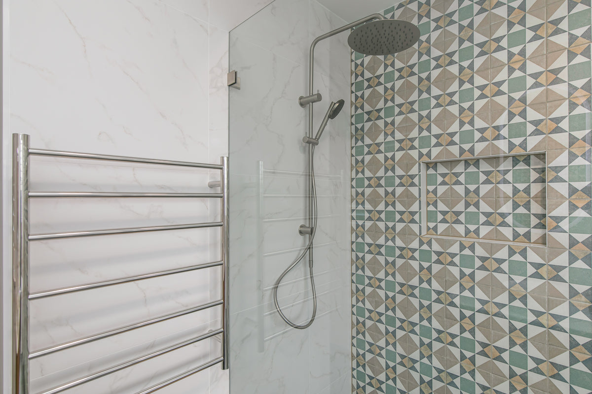 Walk-in shower behind a frameless glass panel, with a rain head, handheld rail shower, brushed nickel tapware and a tiled recessed niche